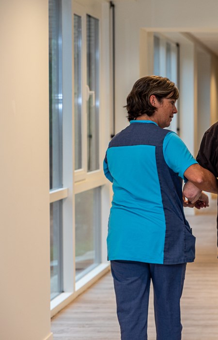 Verpleegkundige wandelt met bewoner van woonzorgcentrum door de gang